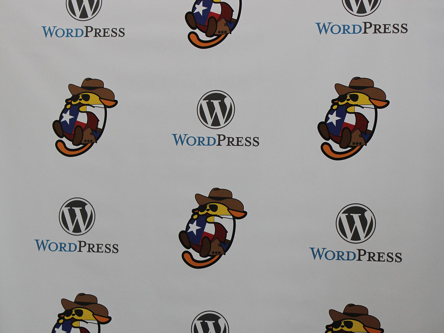 Step and repeat banner with the WordPress logo and the Cowboy Wapuu