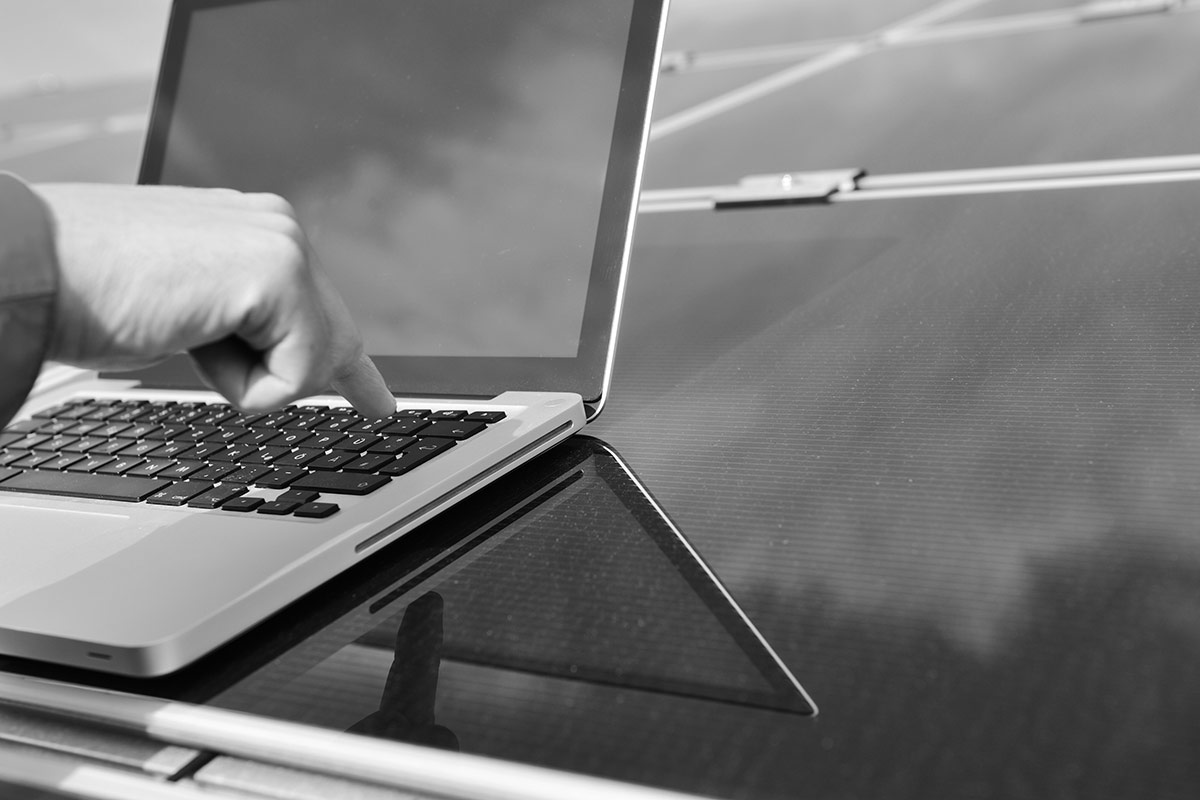 A person pressing a key on a MacBook pro laptop on top of solar panels