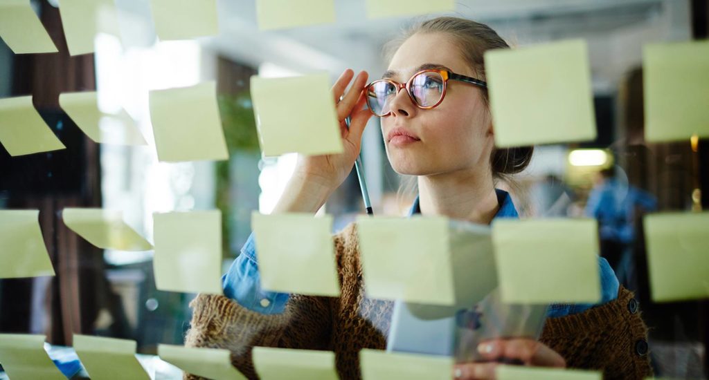 Woman looking at yellow sticky notes on a glass wall