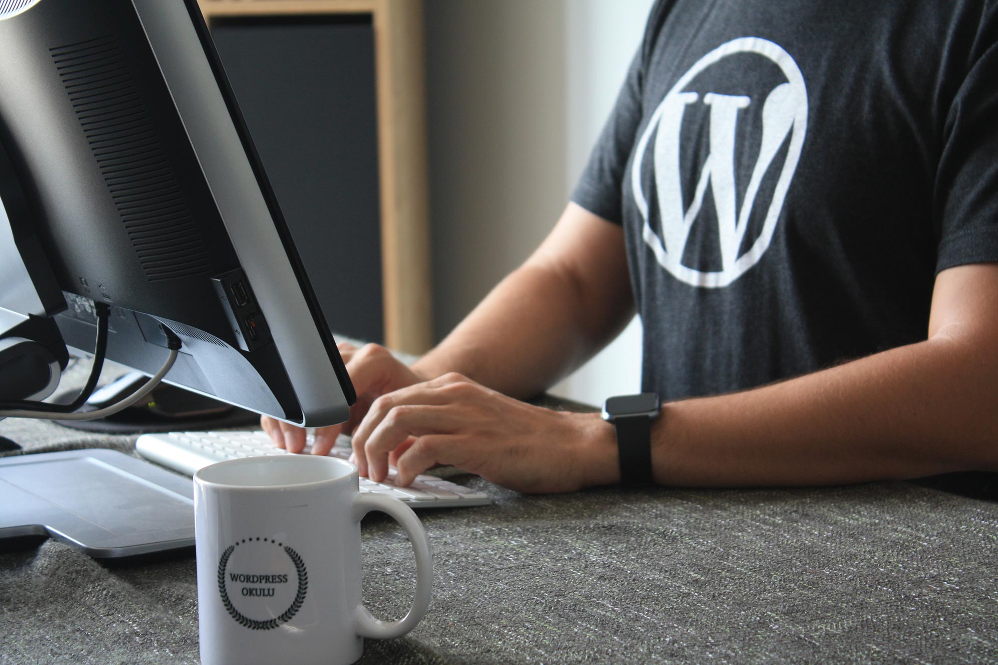 A person wearing a WordPress t-shirt standing at a desk and working on a computer