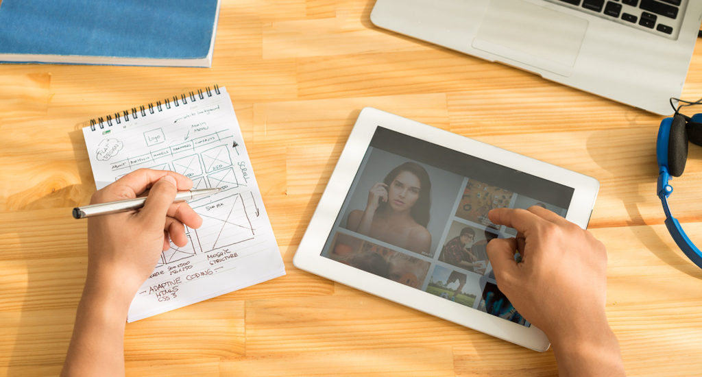 A person sketching on a notebook and looking at a tablet device