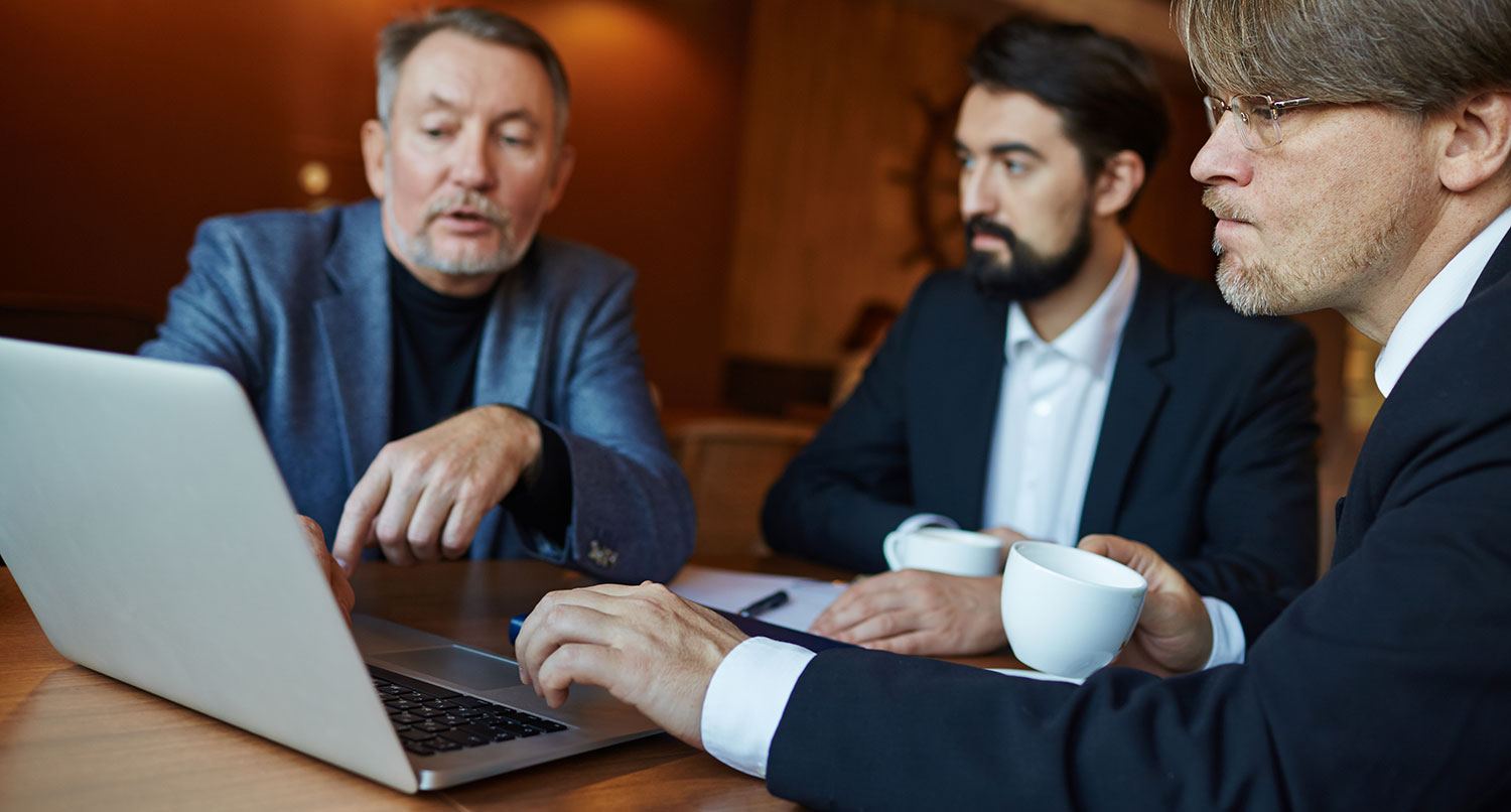 Three men looking over something on a laptop