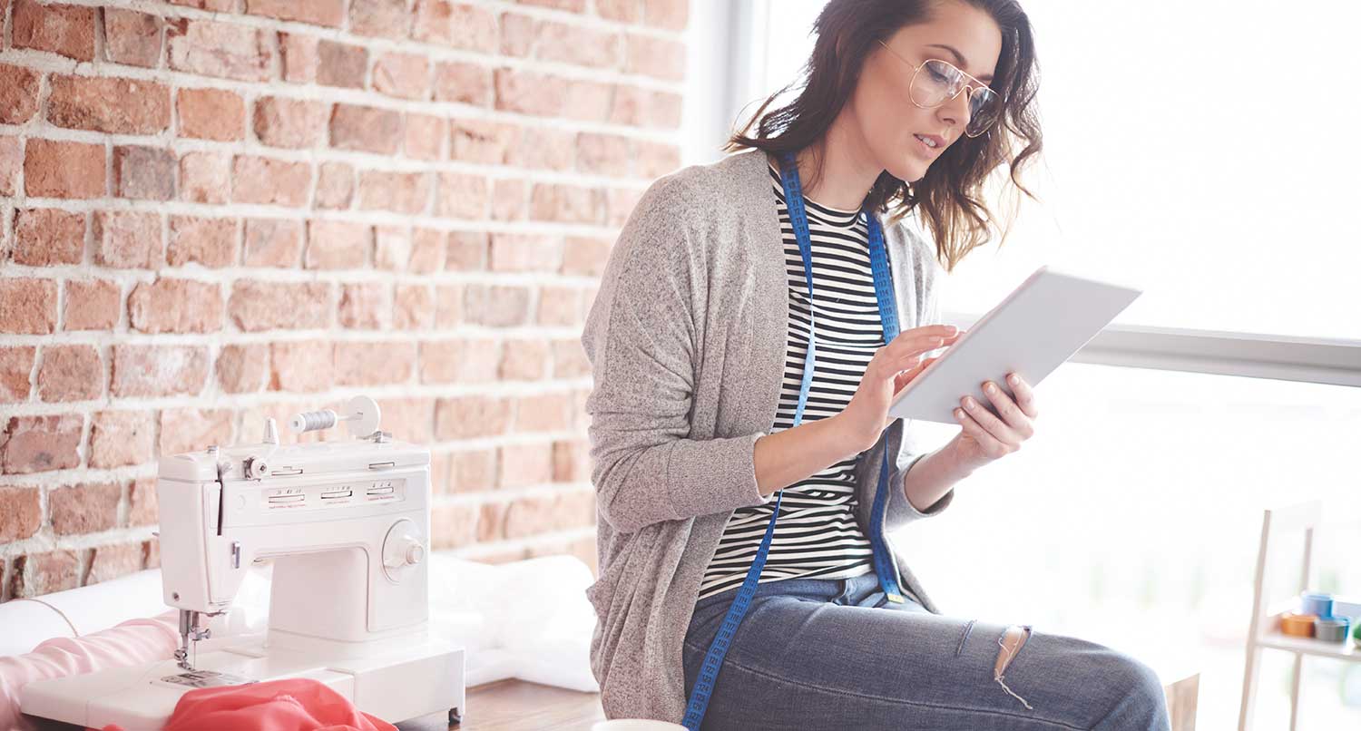 Female small business owner sitting on a table looking at an iPad