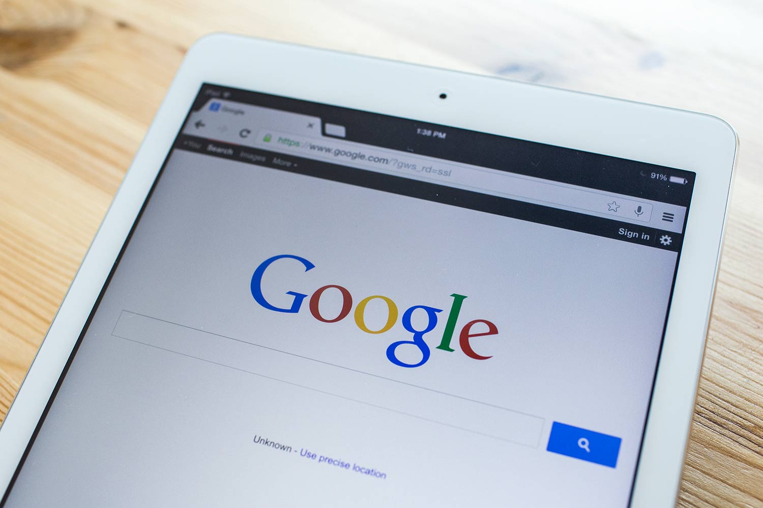 The Google homepage on an iPad resting on a wooden desk