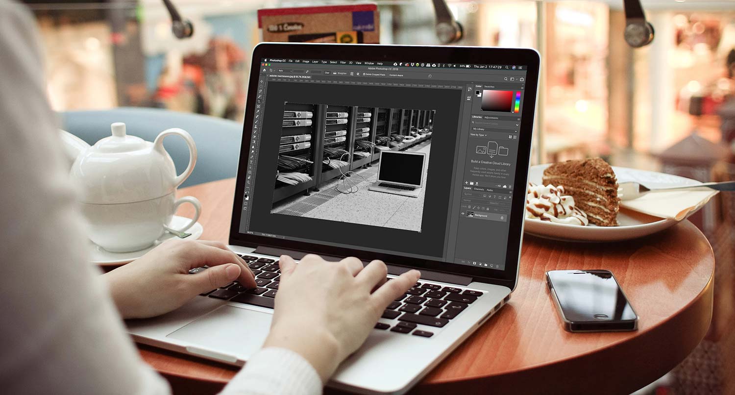An open image in Photoshop on a laptop on a small wooden table in a cafe