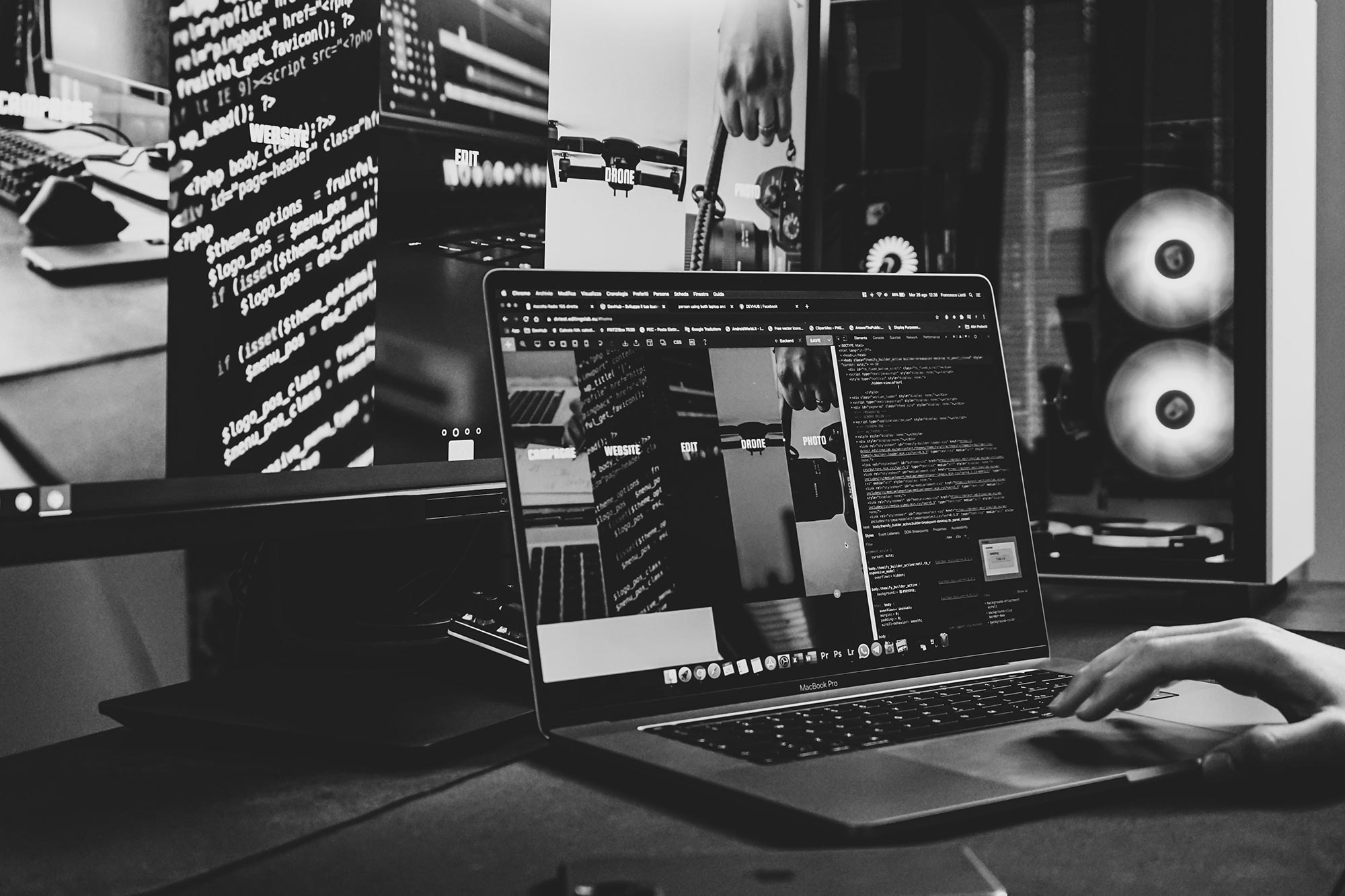 A MacBook sitting in front of a monitor showing a website