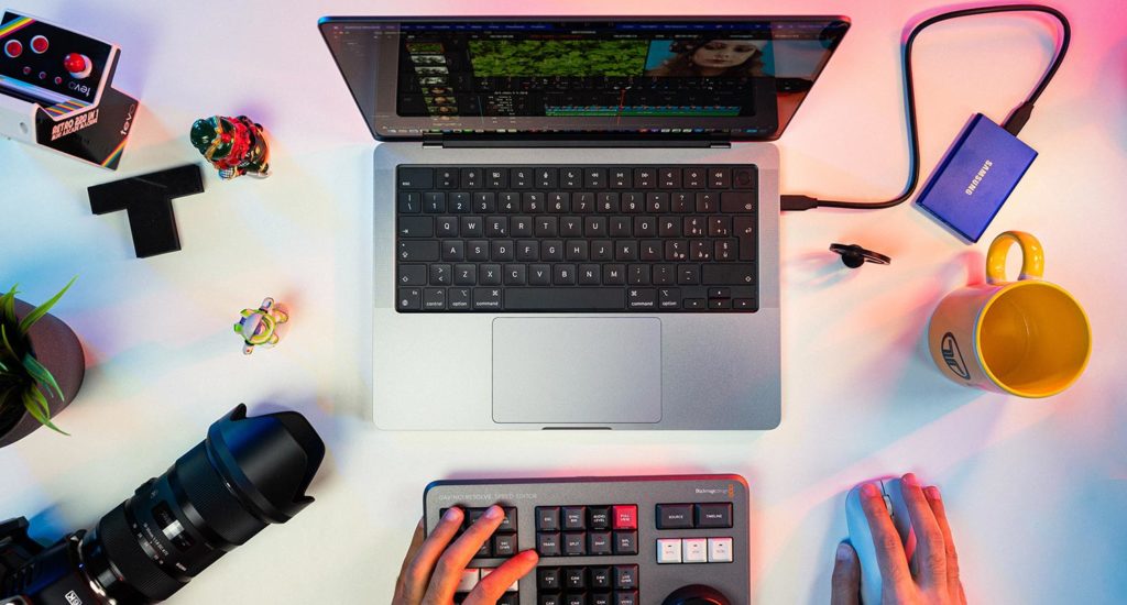 A laptop, camera, stream deck, yellow mug and SD card reader sitting on a while desk