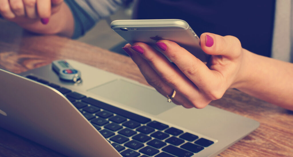 A person holding an iPhone over a MacBook Pro