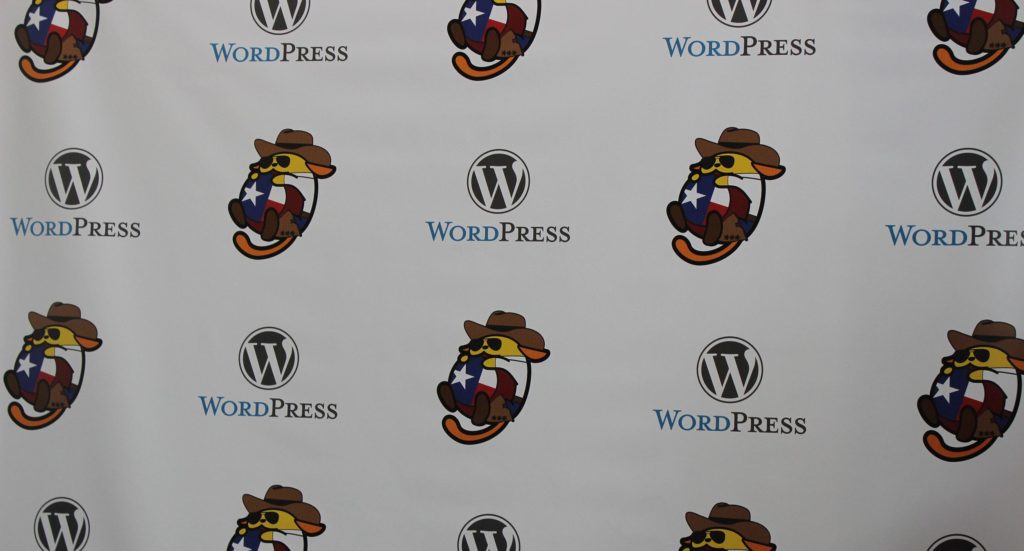 Step and repeat banner with the WordPress logo and the Cowboy Wapuu