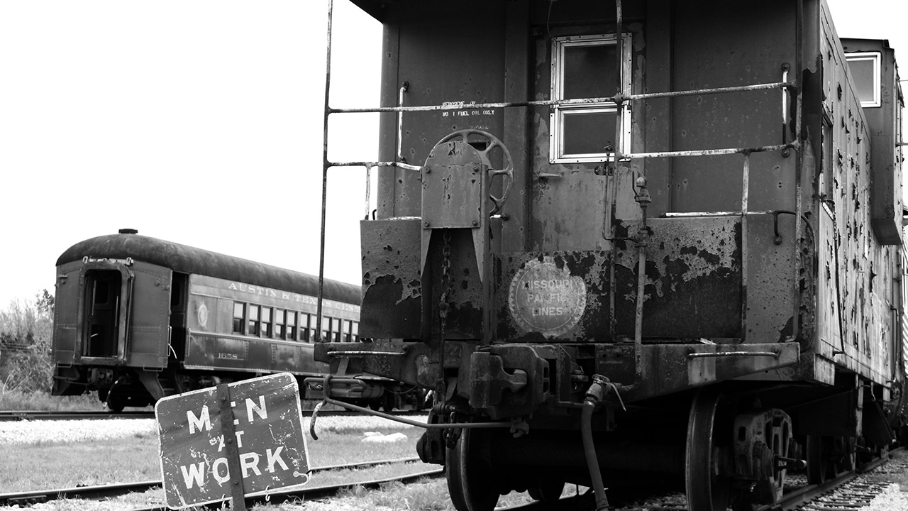 A men at work sign with an aging caboose sitting on the railroad tracks