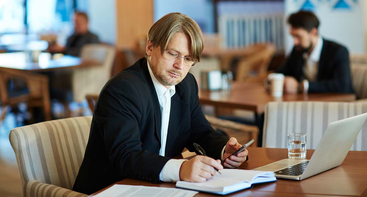 businessman looking at laptop and taking notes in a notebook