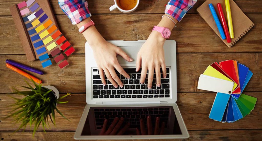Hands of female designer working on laptop at the wooden table