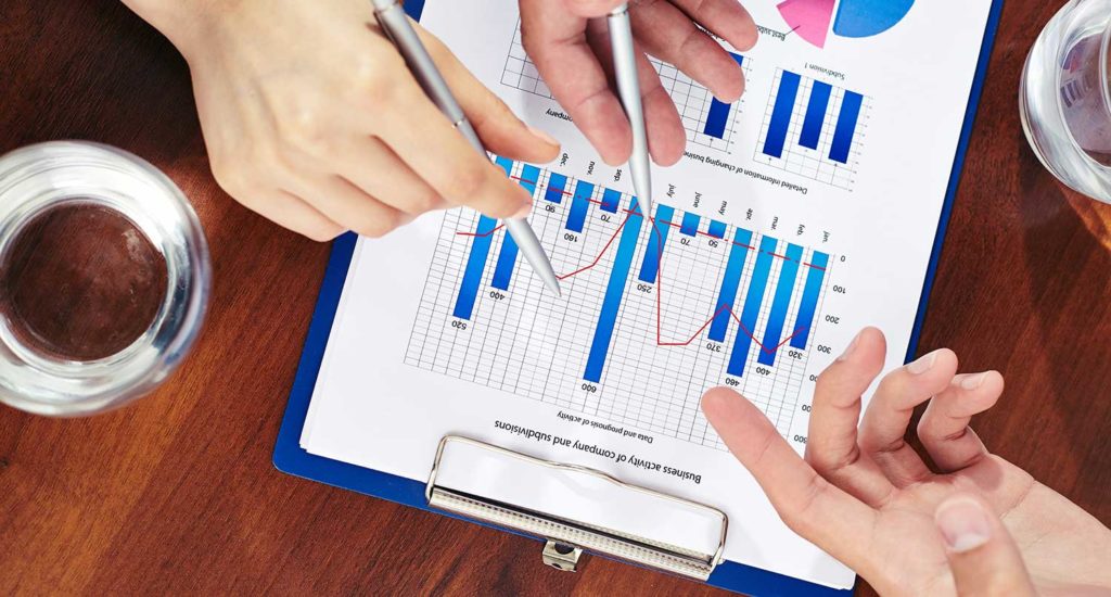 three hands holding pens over top a clipboard with bar graphs on them