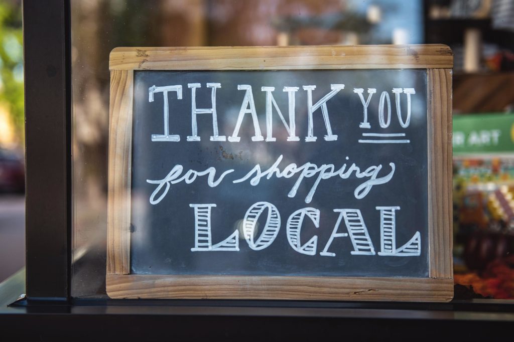 Chalkboard reading "Thank you for shopping local" in a storefront window