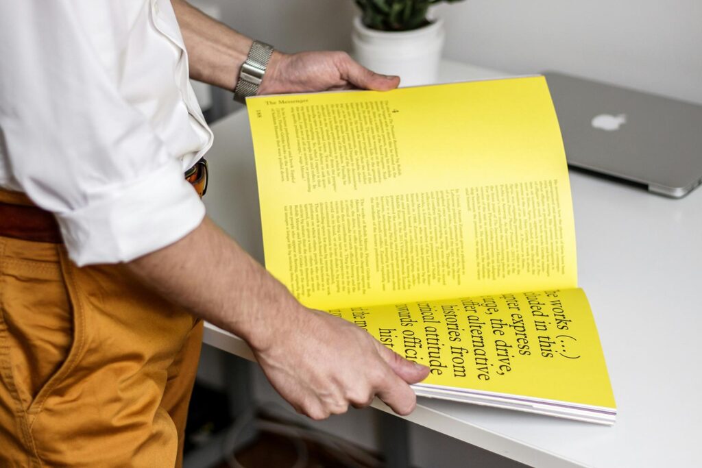 a person holding an open magazine with a yellow page spread