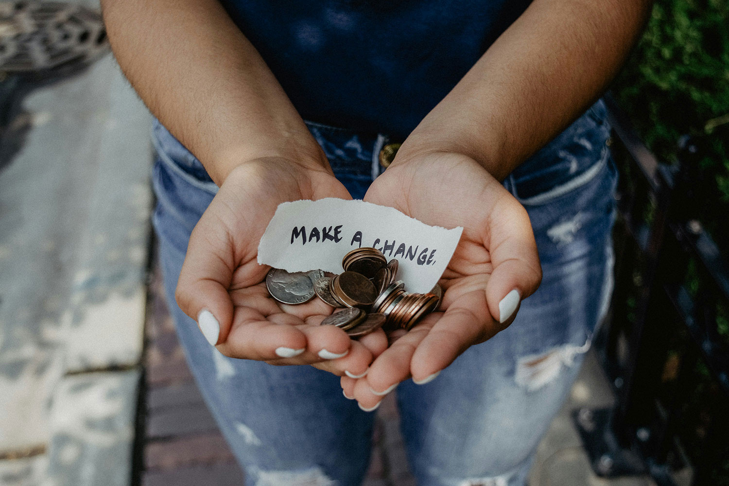 A person holding a number of coins and a piece of paper with "make a change" written on it