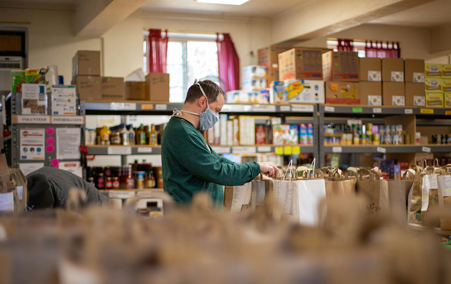 a man wearing a face mask looking at food bags in a food pantry